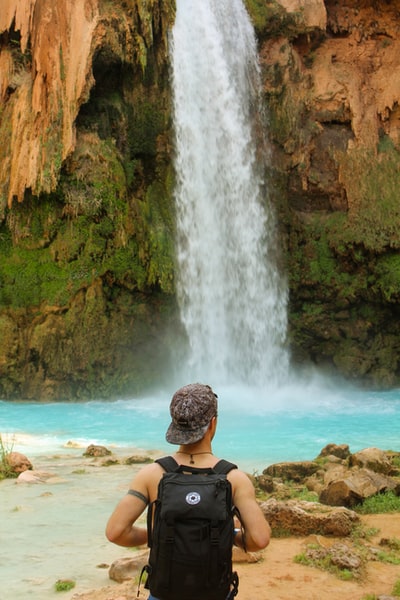 白天，一个穿着黑色比基尼的女人坐在瀑布附近的棕色岩石上